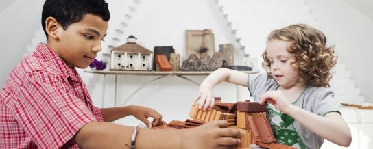 Boy and girl playing with miniature bricks, clay blocks and clay roof tiles in attic loft