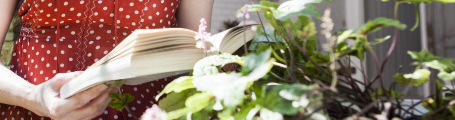 Woman reading a book next to open window in front of brick wall