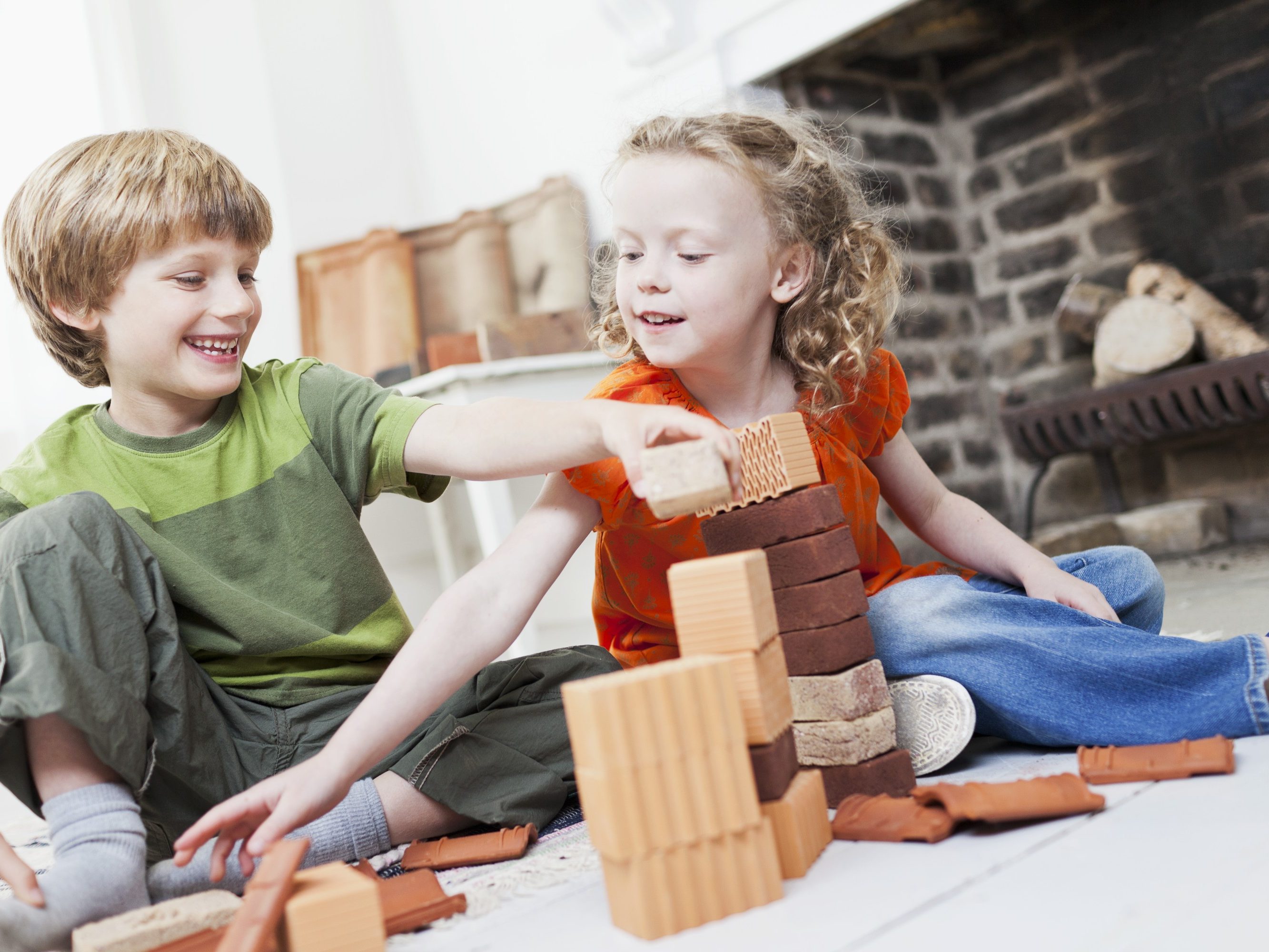 Boy and girl playing with miniature bricks, clay blocks and clay roof tiles in front of fireplace